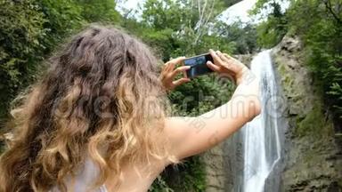 女人把注意力放在智能<strong>手机屏幕</strong>上，拍一张公园瀑布的<strong>照片</strong>